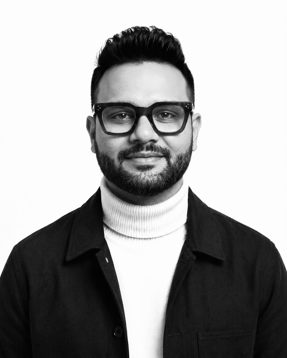Lokesh Mohan, photographed in black and white: dark-rimmed glasses, a white roll-neck and a black overshirt, looking straight at the camera