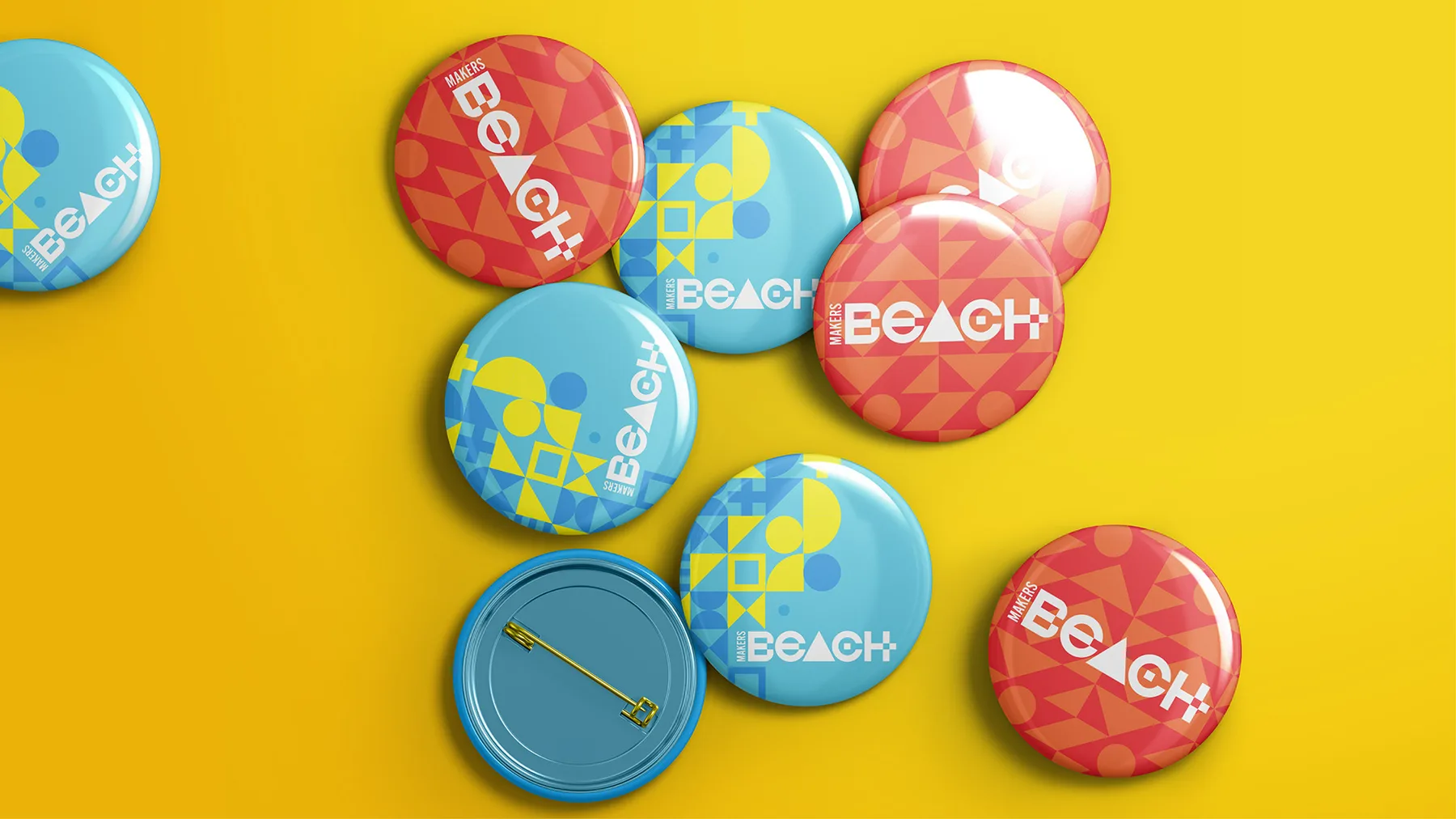 A scatter of Makers Beach pin badges in red and blue colourways